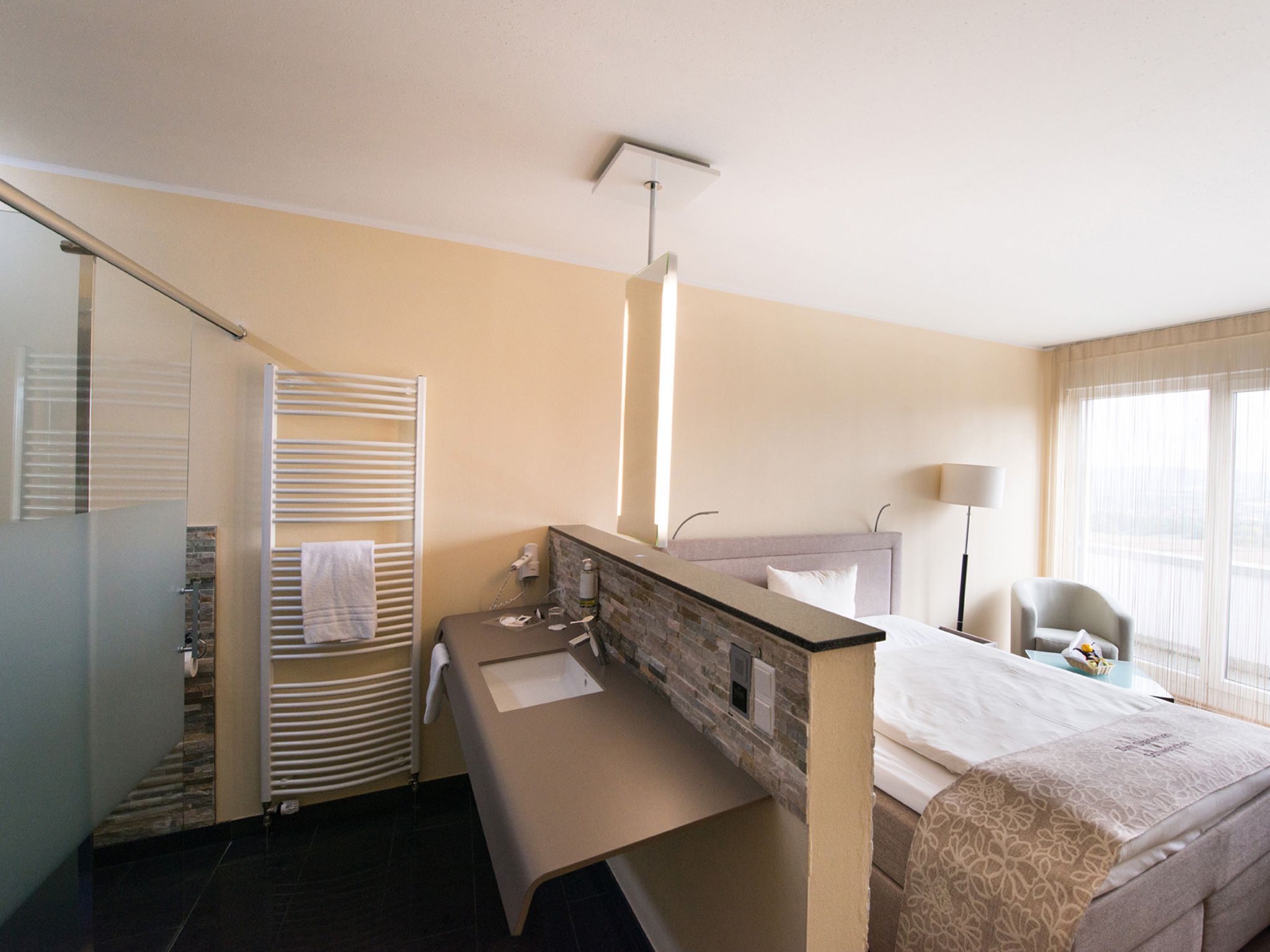 A hotel room with a bed, a desk, a bathroom, and a window with curtains.