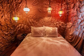 A bed with a tufted headboard, two hanging lanterns, and a small round table with a candle. - Hotel The Exchange (Amsterdam)