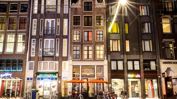 A hotel with a visible entrance, outdoor seating area with umbrellas, and bicycles parked outside. - Hotel The Exchange (Amsterdam)
