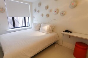 A bedroom with a bed, white pillows, a window, a wall-mounted phone, and a red trash bin. - Hotel The Exchange (Amsterdam)