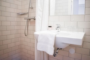 A bathroom with a white sink, a shower, and a mirror. - Hotel The Exchange (Amsterdam)