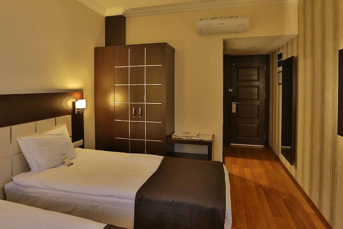 A hotel room with two beds, a wardrobe, a bedside table, and a door leading to another room.