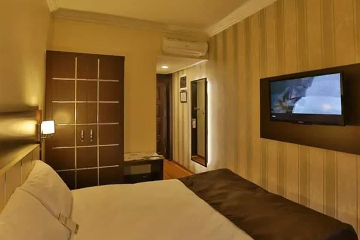 Habitación de hotel con cama, televisor montado en la pared, puerta y equipo de aire acondicionado.