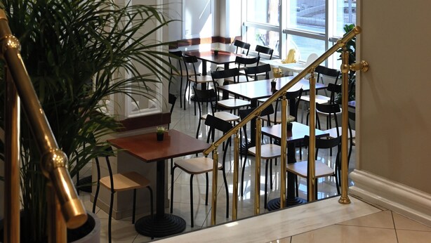 A hotel lobby with a staircase, seating area, and a large potted plant. - Achillion Hotel (Larissa)