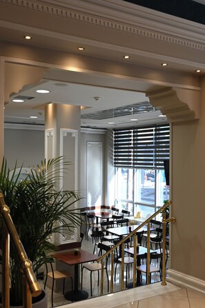A hotel lobby with a staircase, seating area, and a large potted plant. - Achillion Hotel (Larissa)