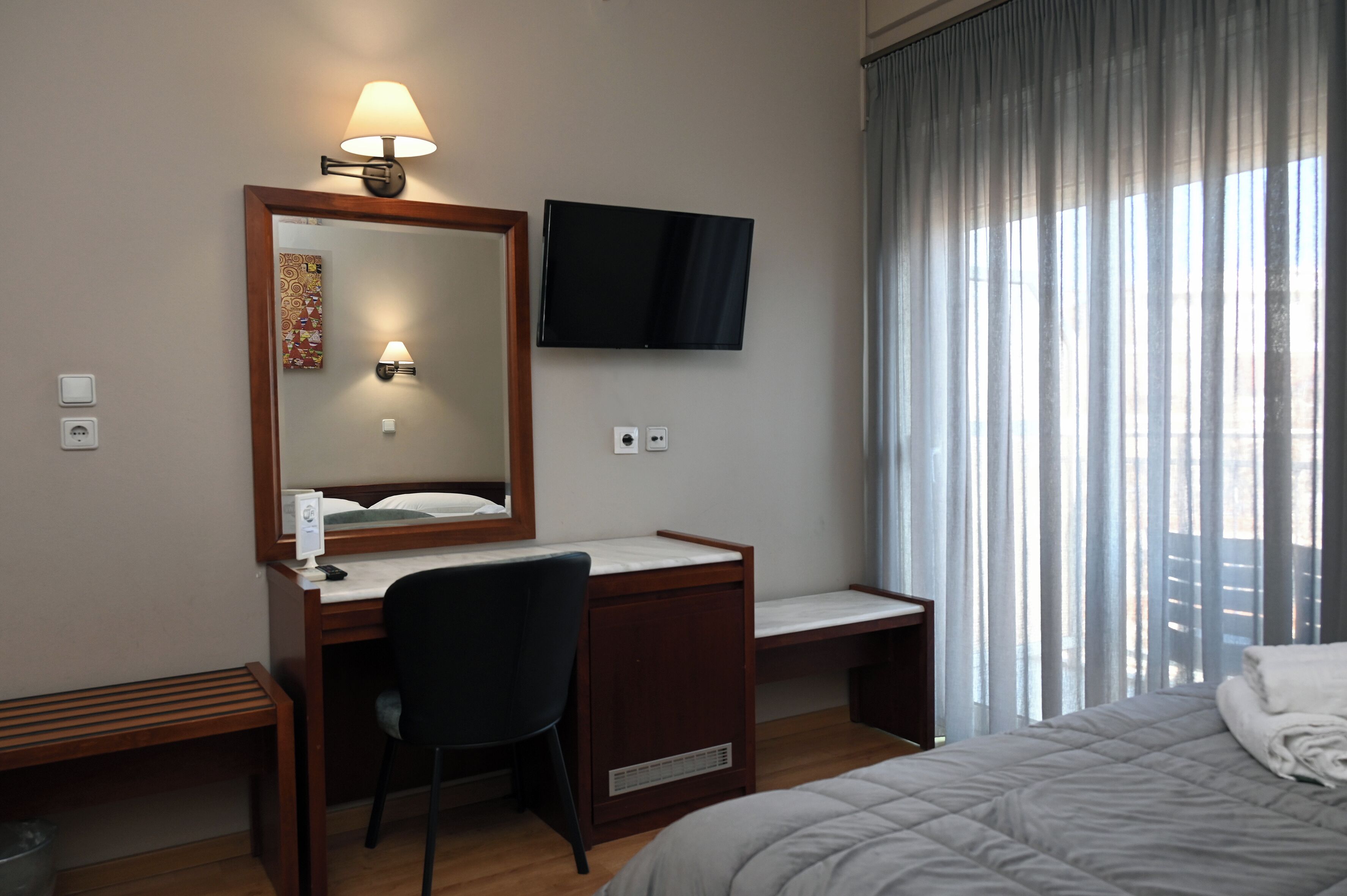 Habitación de hotel con cama, escritorio con silla, televisor, espejo y ventana con cortinas.