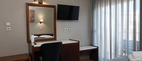 Habitación de hotel con cama, escritorio con silla, televisor, espejo y ventana con cortinas.