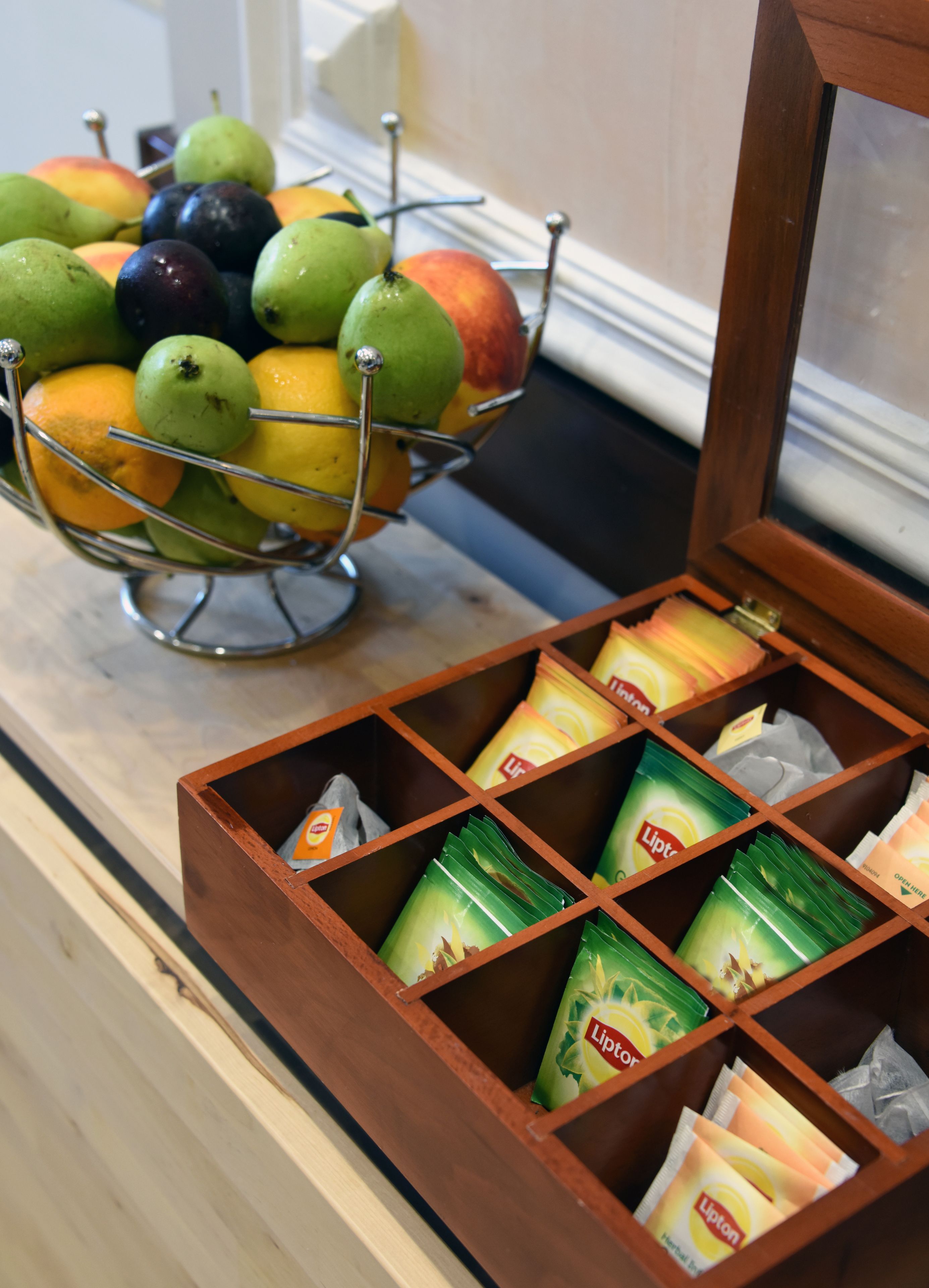 A fruit bowl with apples and oranges on a counter next to a drawer with Lipton tea packets.