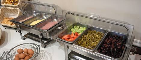 Een buffet met diverse soorten eten, zoals eieren, ham, groenten, olijven en bonen.