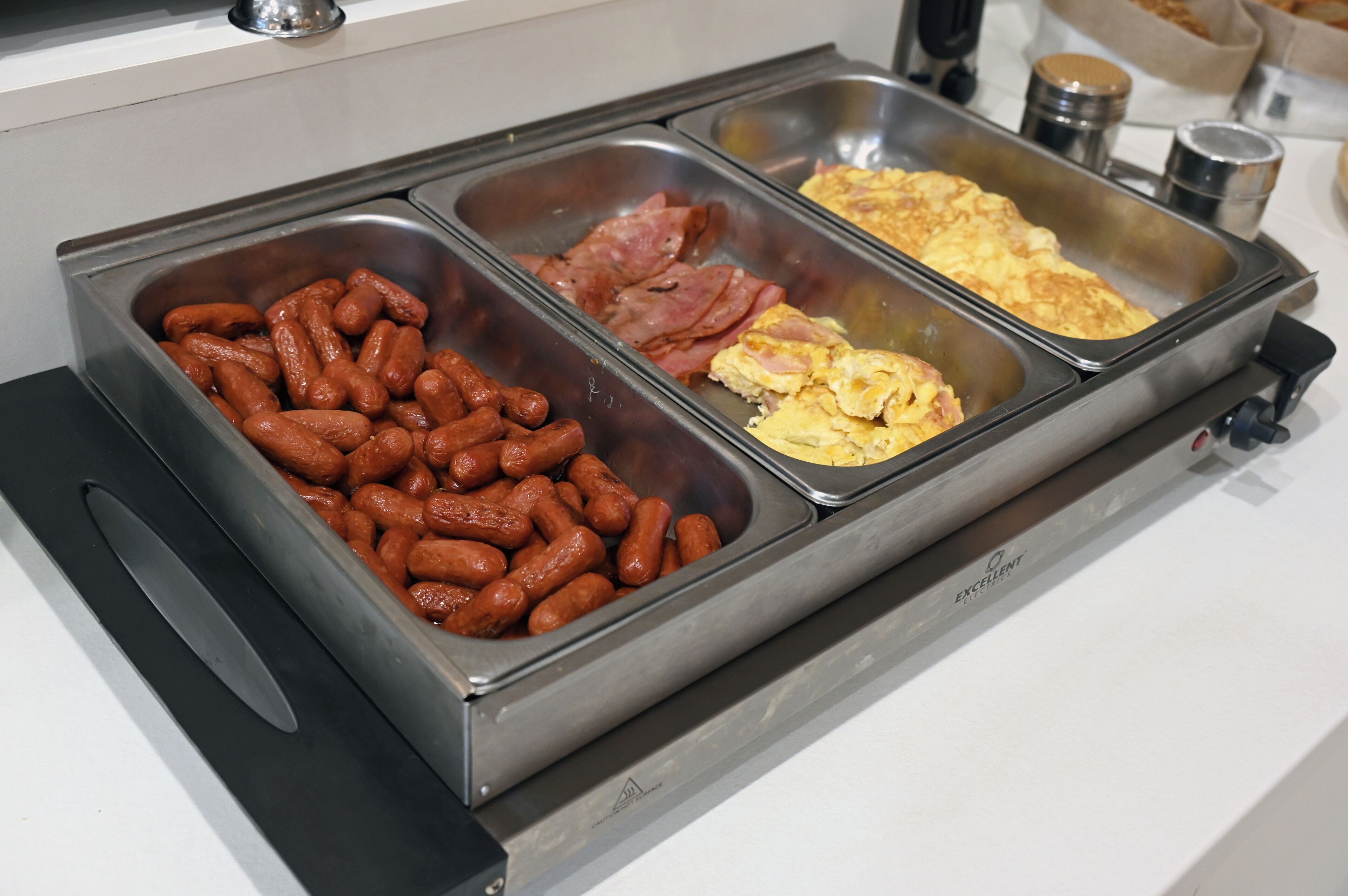 Een buffet met drie opschepbakken: worst, ham en roerei.
