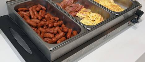 A buffet with three food trays: sausages, ham, and scrambled eggs.