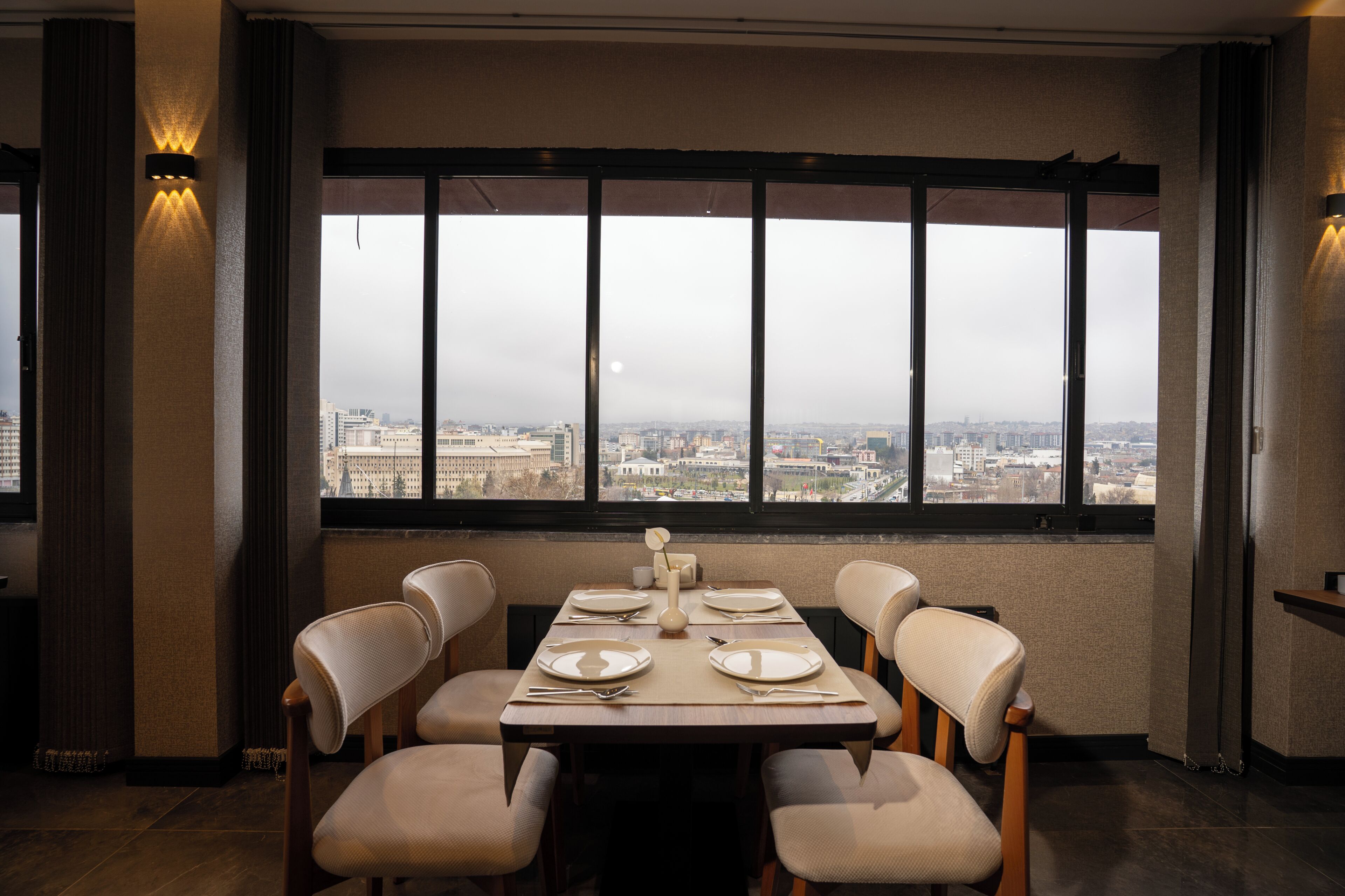 Un espace repas avec une table dressée pour six personnes, de grandes fenêtres offrant une vue sur la ville et un aménagement intérieur moderne.