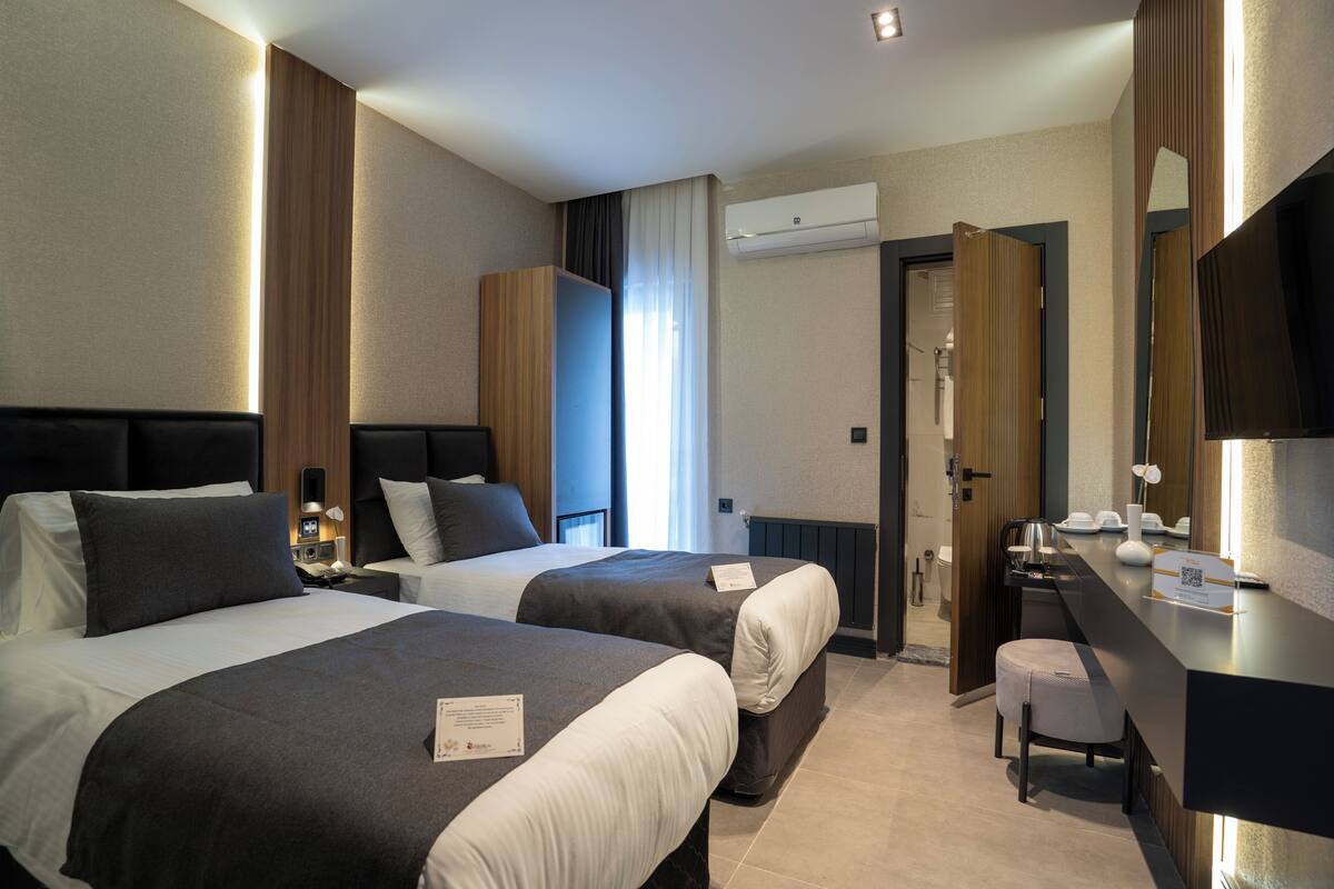 A hotel room with two beds, a desk, a chair, an air conditioning unit, and a mirror.