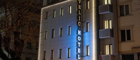 Un hotel de varios pisos con un letrero llamativo, una tienda de televisores y una tienda cerrada.