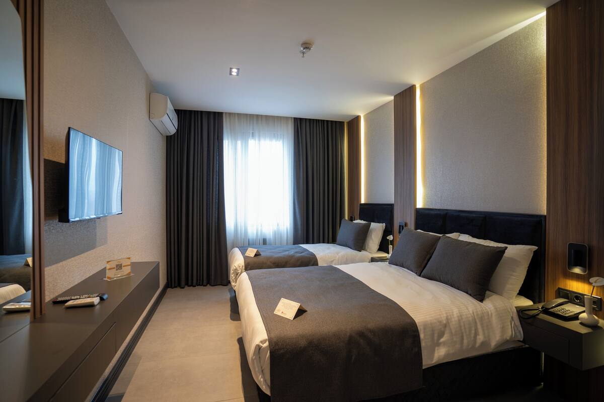 A hotel room with two beds, a flat-screen TV, a desk with a remote control, and a bedside table with a lamp.