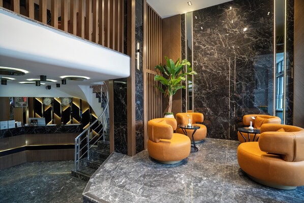 Vestíbulo con mostrador de recepción, zona de estar, escalera y un espejo grande que refleja el interior.
