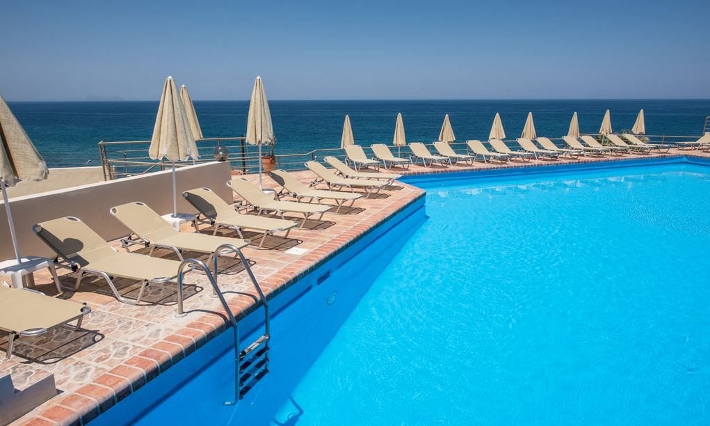 A poolside area with sun loungers and umbrellas, a clear blue pool, and a view of the ocean.