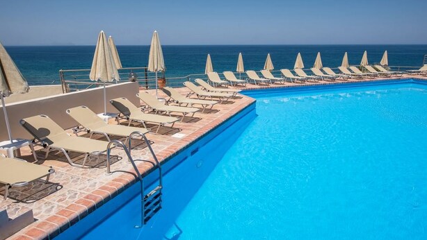 A poolside area with sun loungers and umbrellas, a clear blue pool, and a view of the ocean. - Scaleta Beach (Rethymno)