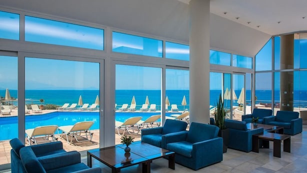 A spacious indoor area with large windows offering a view of a pool and beach chairs. - Scaleta Beach (Rethymno)