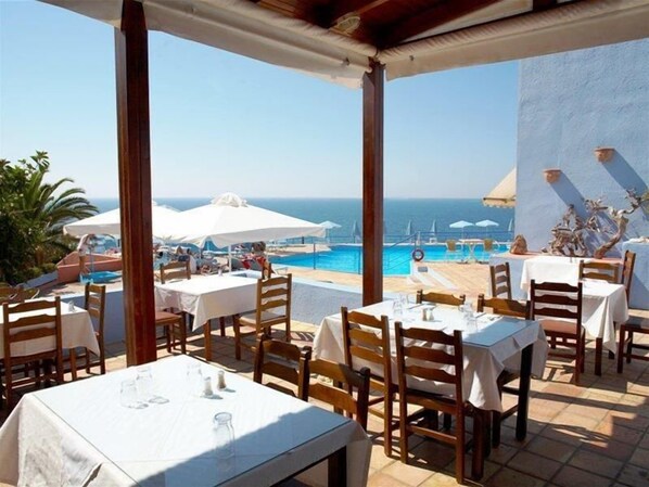 An outdoor dining area with tables and chairs, overlooking a pool and the sea. - Scaleta Beach (Rethymno)