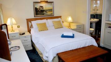 A neatly arranged hotel room with a bed, bedside tables, a desk, and a bathroom visible through an open door.