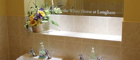 Une salle de bain avec deux lavabos, un miroir et un vase rempli de fleurs.