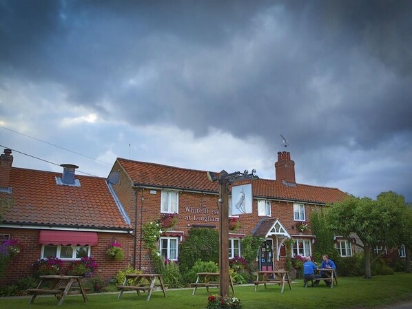 Un pub tradicional con techo de tejas rojas, mesas al aire libre y un cartel que dice "The White Horse at Longnams".