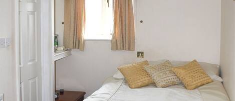A bedroom with a bed, pillows, a window with curtains, a bedside table, and a wall-mounted light fixture.