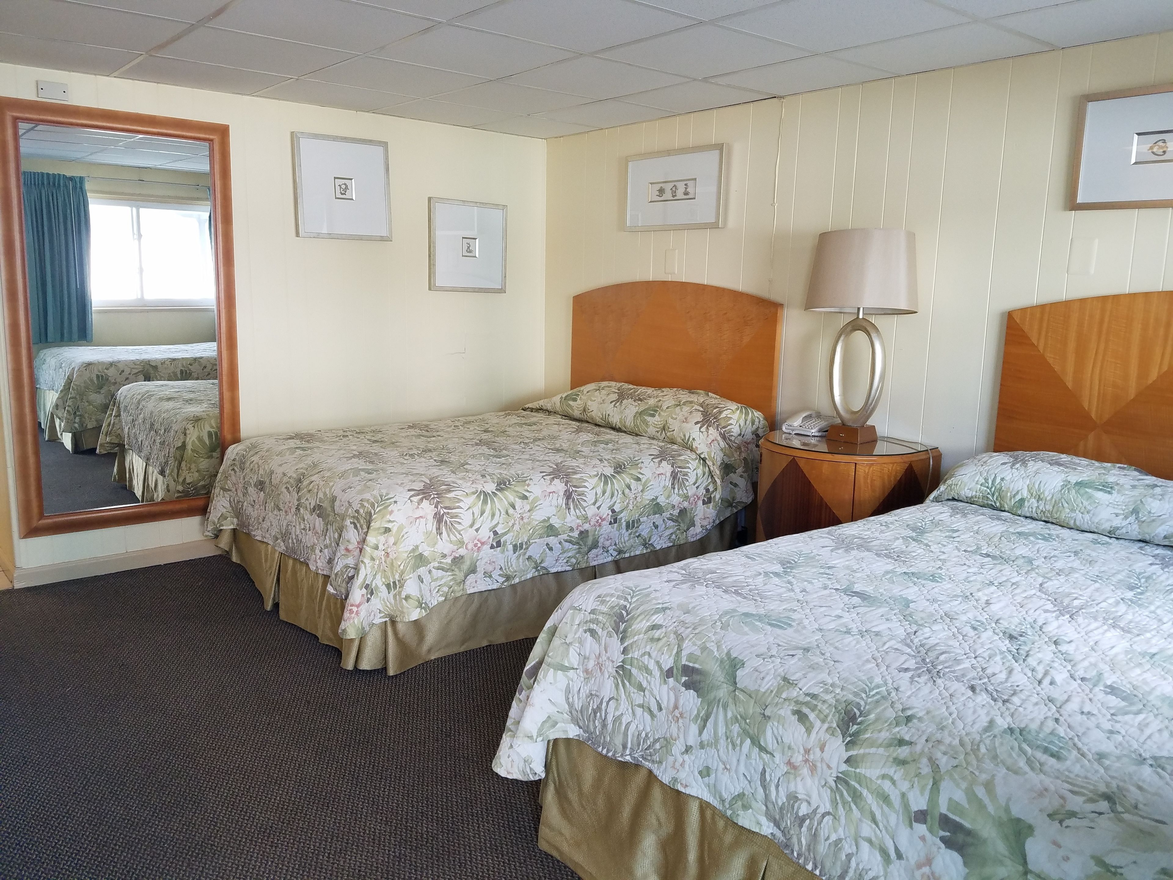 A hotel room with two single beds, a wooden headboard, a bedside table with a lamp, and a mirror.