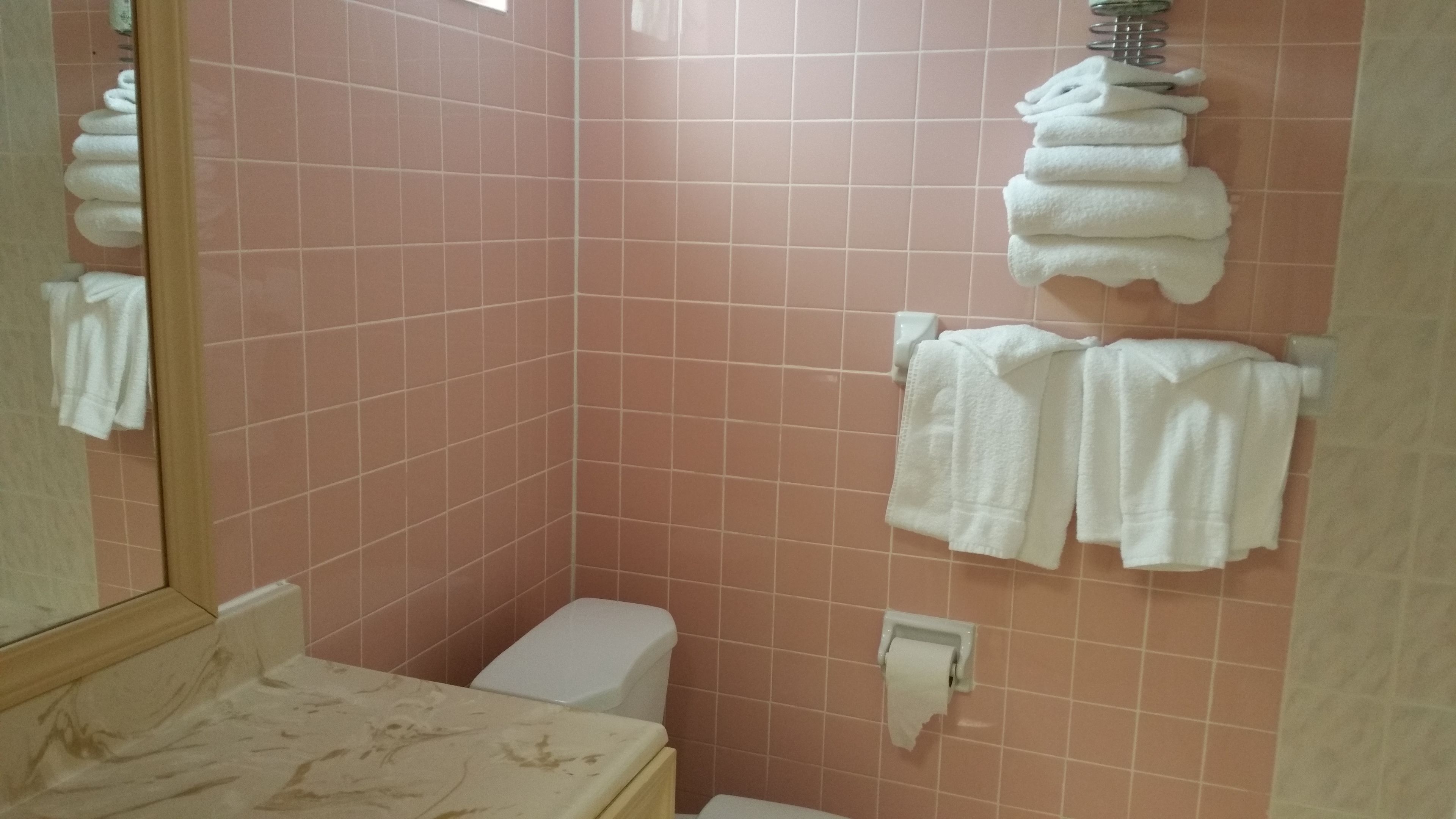 Ein Badezimmer mit rosafarbenen Fliesen, einer Toilette, einem Waschbecken mit Marmorplatte und Handtüchern, die an der Wand hängen.