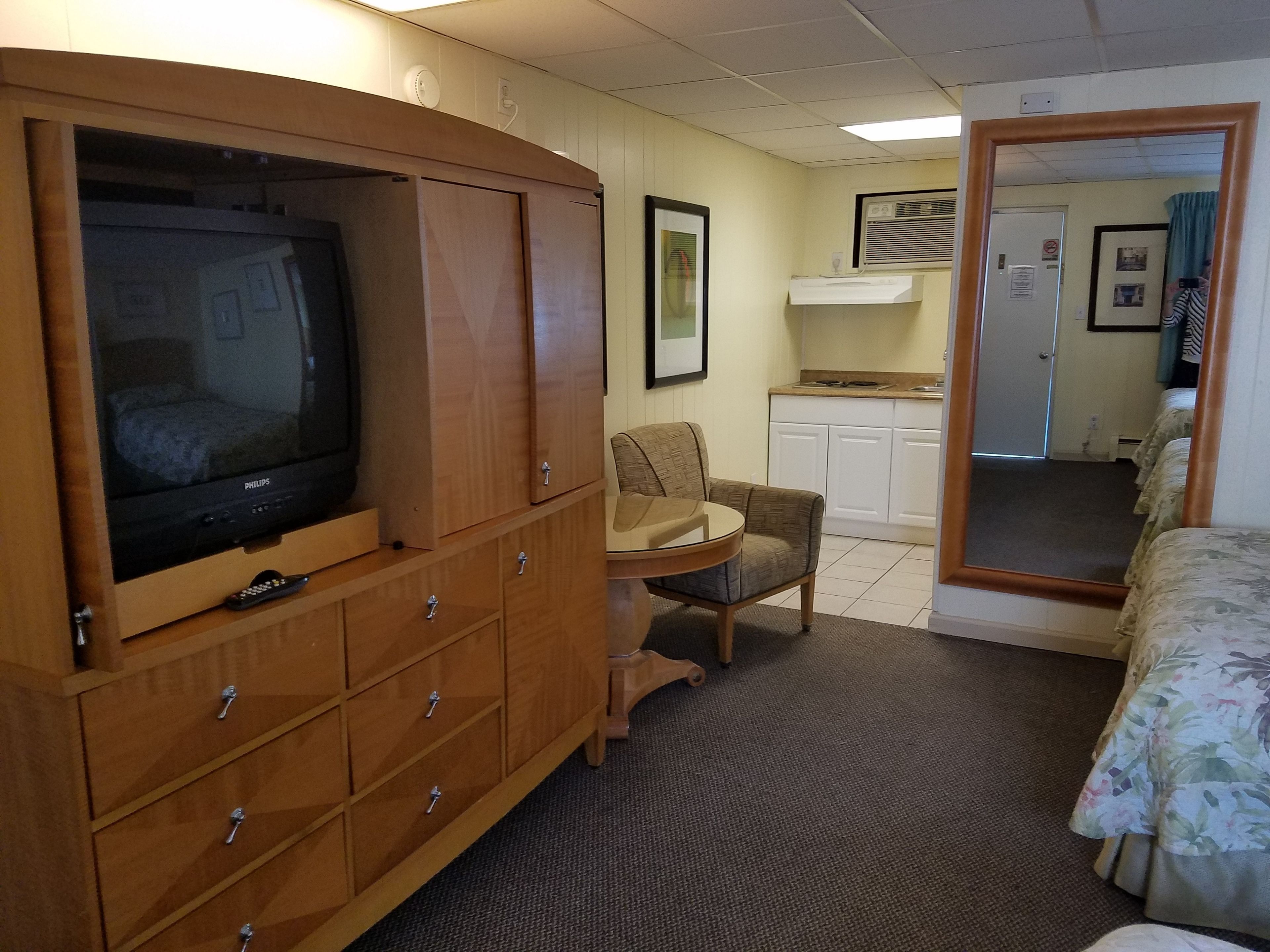Una camera d'albergo compatta con televisione, angolo cottura, una sedia e un letto.