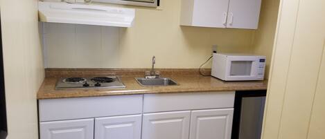 A compact kitchen with white cabinets, a gas stove, a sink, a microwave, and a vent above the stove.
