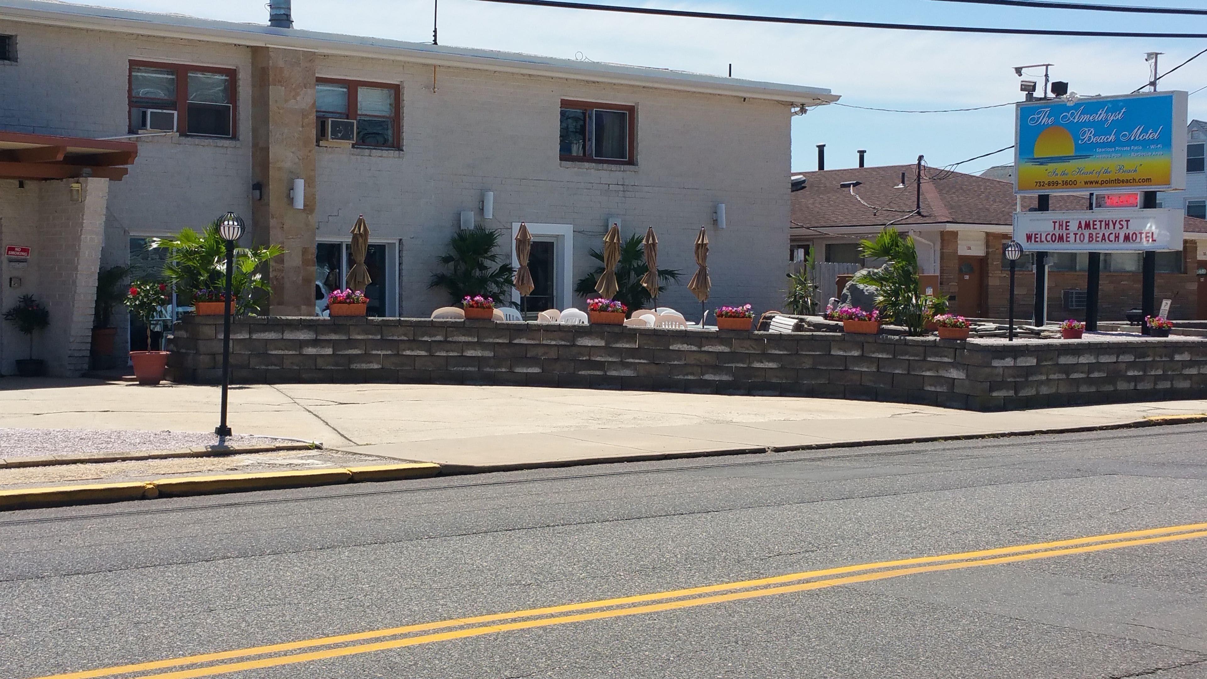 Un motel à l’apparence simple, doté d’un espace extérieur avec des tables et des parasols, et offrant une vue dégagée sur la rue.