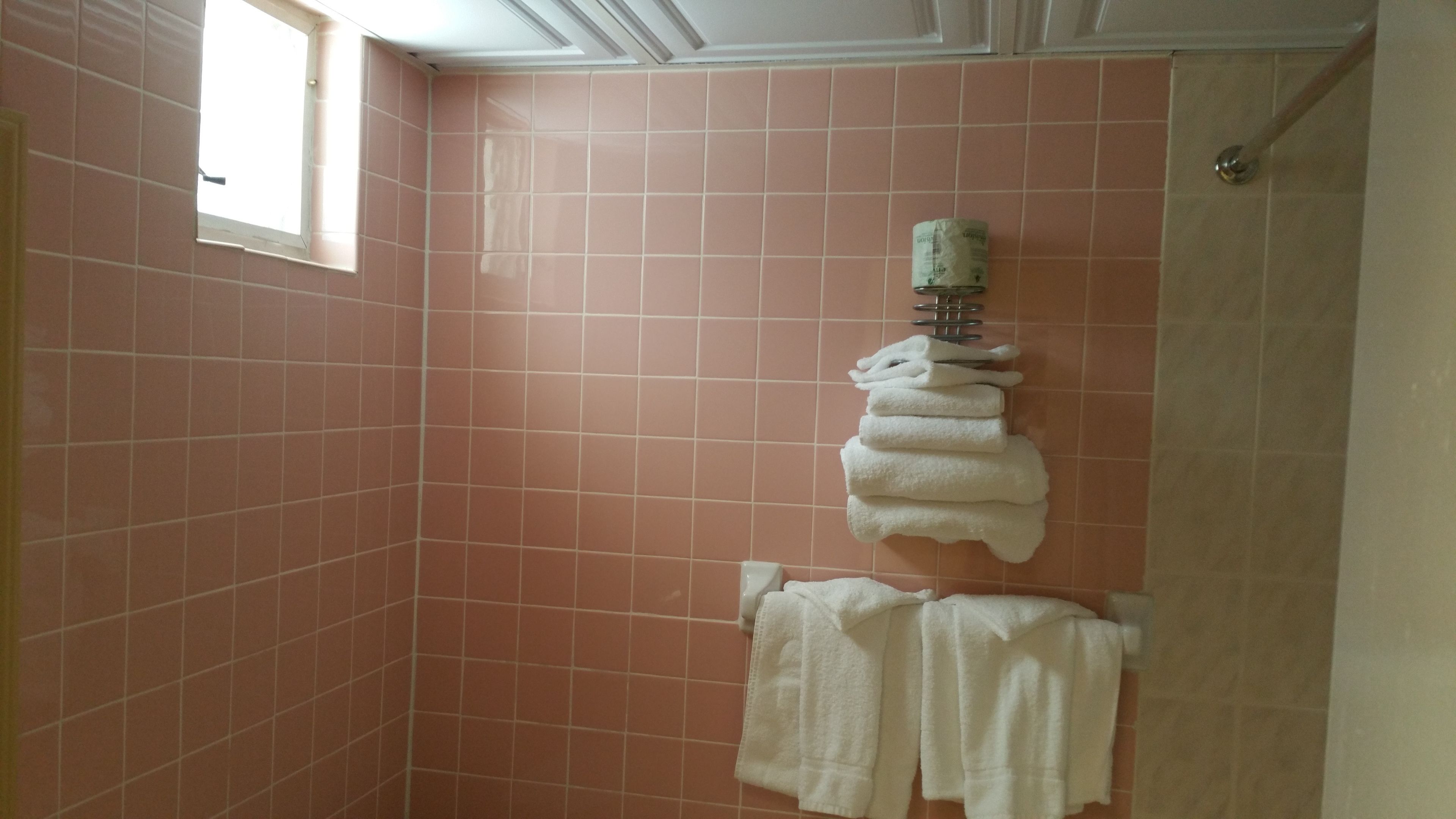 A bathroom with pink tiles, a towel rack with folded towels, and a window.