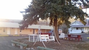 A playground with swings and a picnic table, surrounded by buildings. - Riverside Motel (Helper)