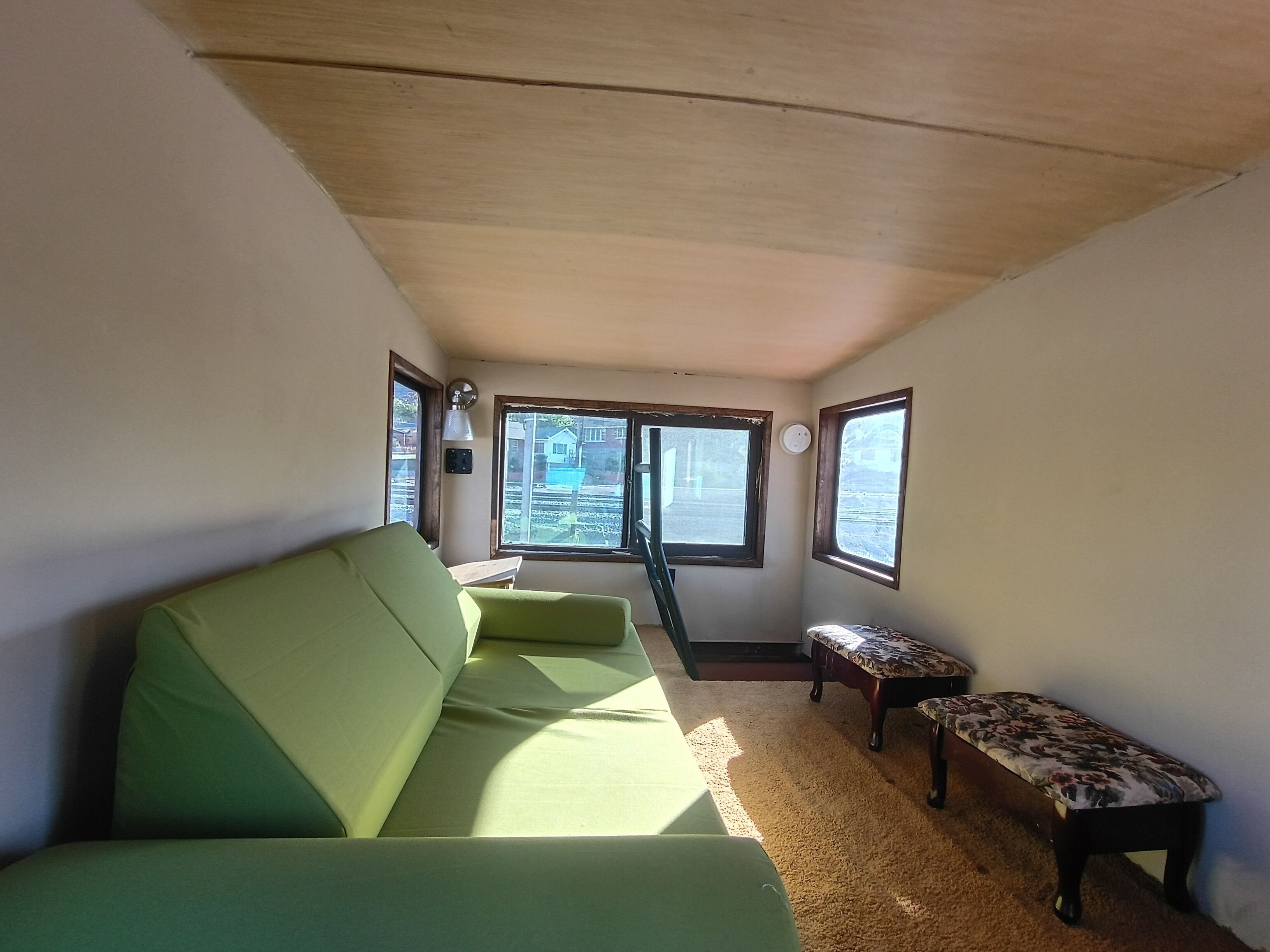 A room with a green sofa, a small table, and two windows providing a view outside.