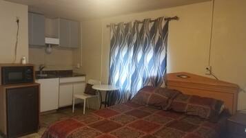 A compact room with a bed, a small kitchenette, a dining table, and a patterned curtain.