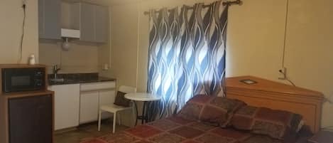 Une pièce de taille modeste comprenant un lit, une petite kitchenette, une table à manger et un rideau à motifs.