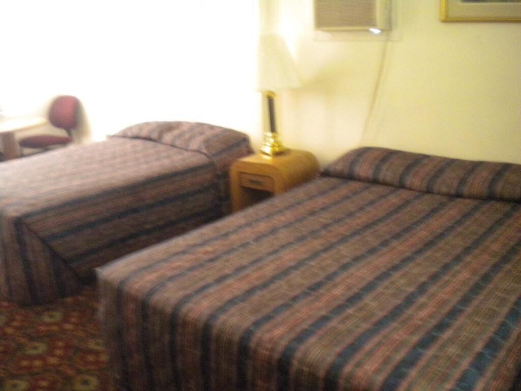 Una habitación de hotel con dos camas, una mesita de noche, una lámpara y una silla.