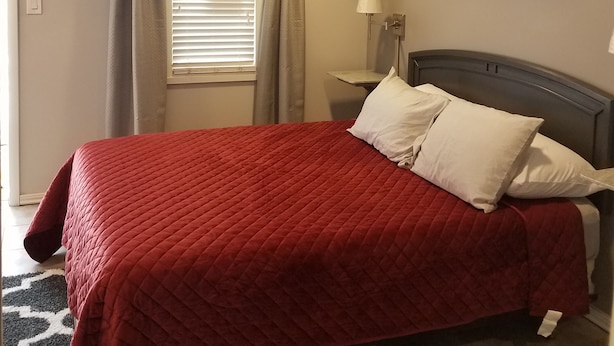 A bedroom with a bed, a nightstand, a lamp, and a window with curtains. - Riverside Motel (Helper)