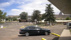 A parking lot with a black car parked near a building with a basketball hoop. - Riverside Motel (Helper)