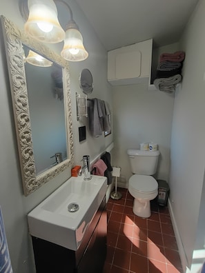 A compact bathroom with a white sink, a mirror with ornate frame, a toilet, and a towel rack.