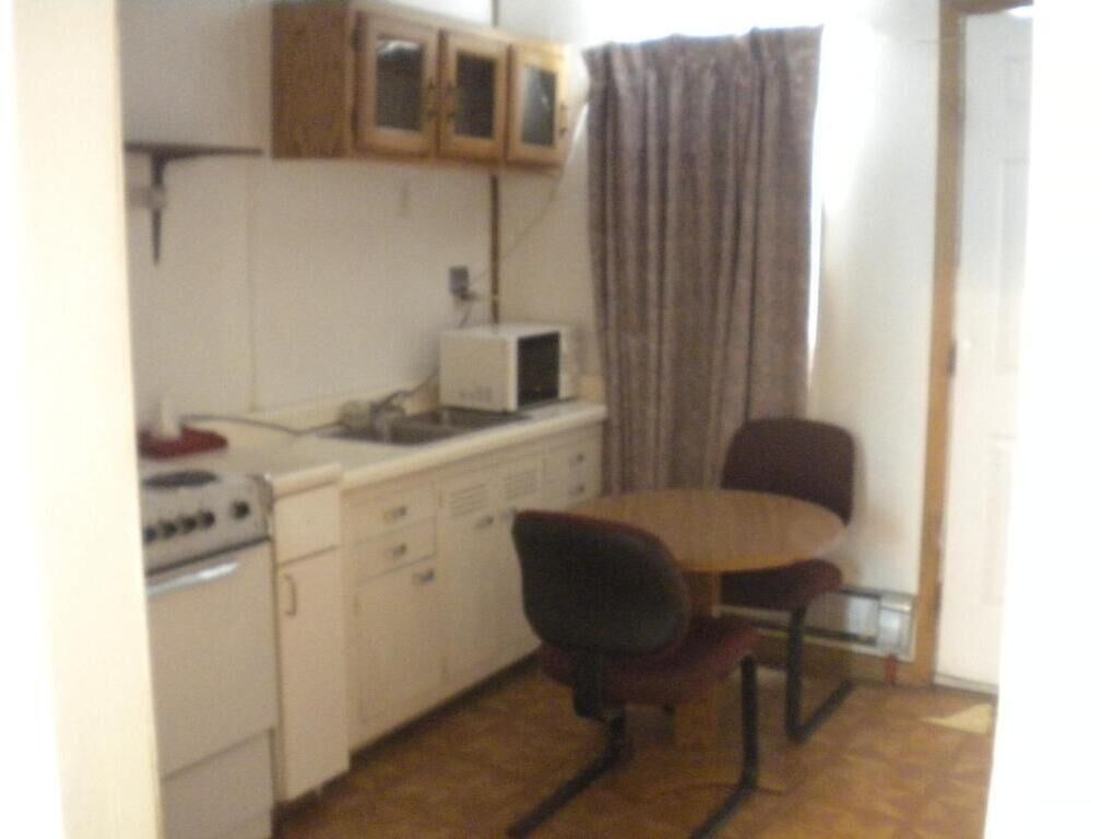 A small kitchen with a microwave, stove, and cabinets. There is a dining table with two chairs.