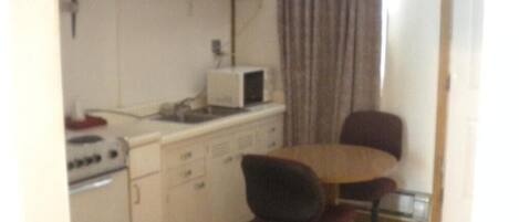 A small kitchen with a microwave, stove, and cabinets. There is a dining table with two chairs.