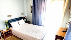 Una cama bien hecha con una colcha estampada, una mesita de noche con lámpara, una silla y una pequeña mesa con un jarrón de flores.