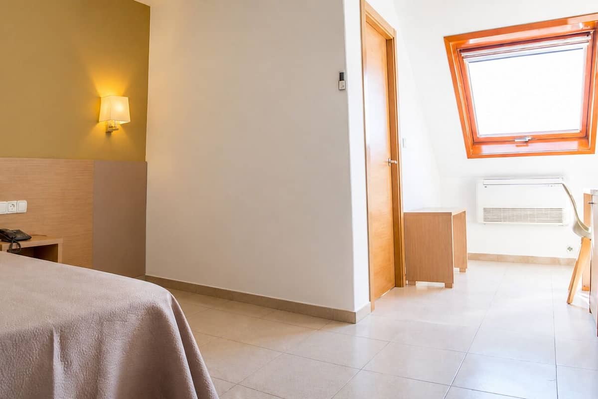 A hotel room with a bed, bedside table, lamp, and a window with a view.