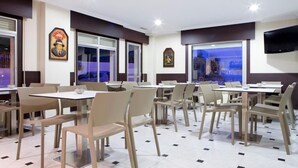 A dining area with tables and chairs, a large window, and a mounted television. - Duna Hotel (Sanxenxo)