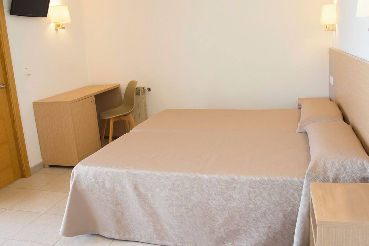 A bedroom with a bed, a desk, a chair, and a TV mounted on the wall.