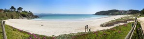 A beach with a clear view of the sea, a sandy shore, and a few buildings in the background. - Duna Hotel (Sanxenxo)