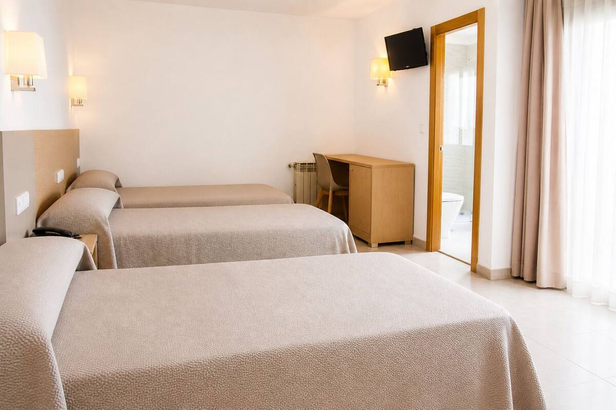 A hotel room with two beds, a desk, a chair, a TV, and a sliding glass door.